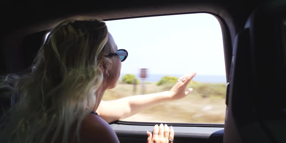 Blonde female passenger reaches hand out of vehicle during a road trip