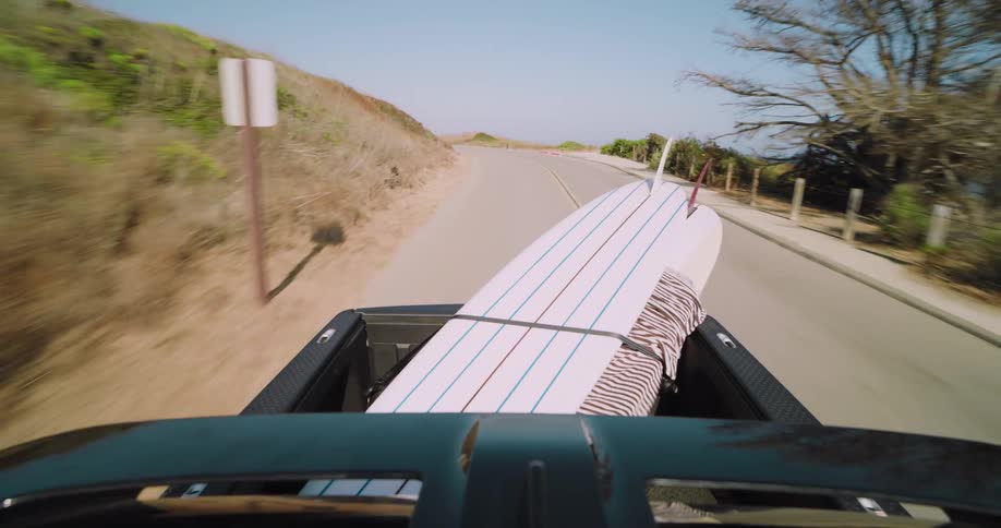 View from the back of a moving vehicle showing surfboards secured in the bed next to the coast