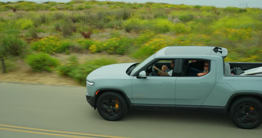 Aerial view of a pickup truck carrying surfboards on a road next to the coast