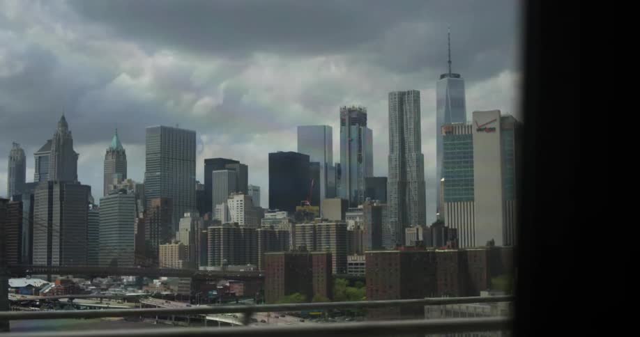A vehicle drives across a bridge with skyscrapers in the background