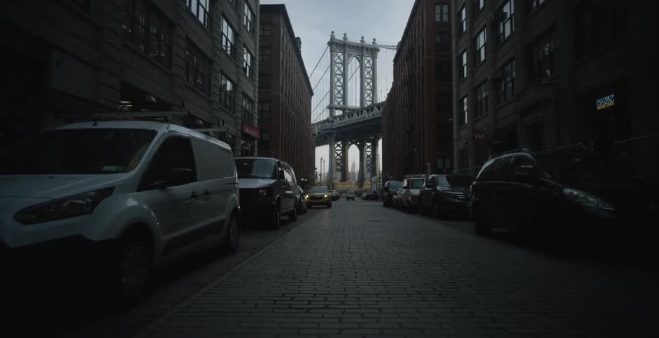 A view of a city street with buildings and cars lines up along both sides of the road