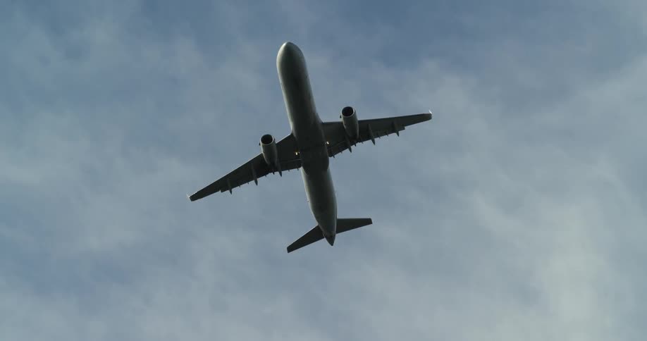 A plane flies on a partly cloudy day