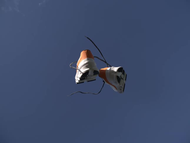 A pair of sneakers tied together is falling from the blue sky
