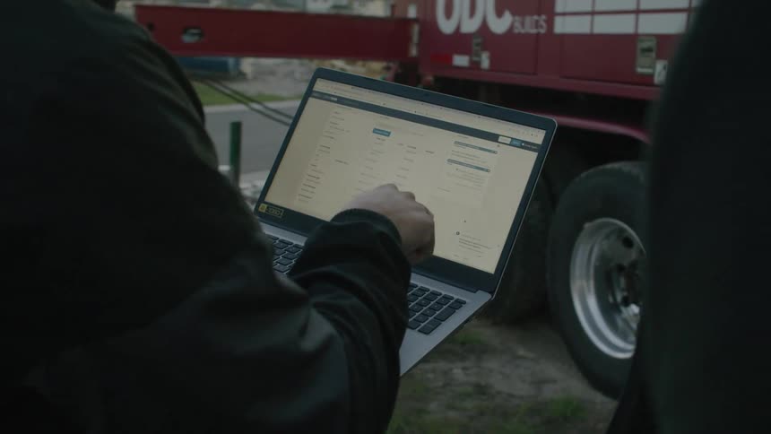 Coworkers consult laptop while standing near heavy duty vehicle with its stabilizing support arms extended