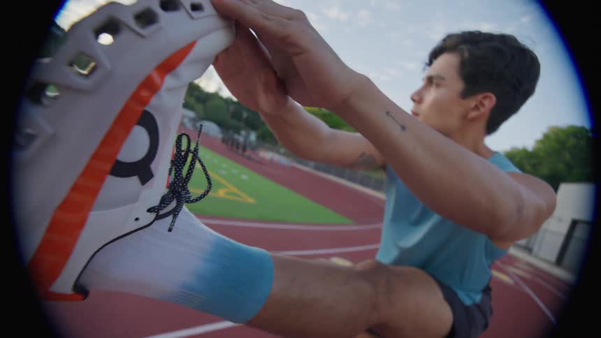 A young man is stretching his leg by placing it upwards on a flat surface of a running track
