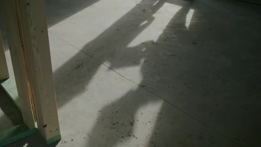 A persons shadow on a concrete floor with wooden and metal structures