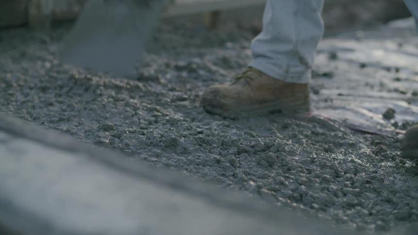A person cementing the ground with a shovel at a construction site