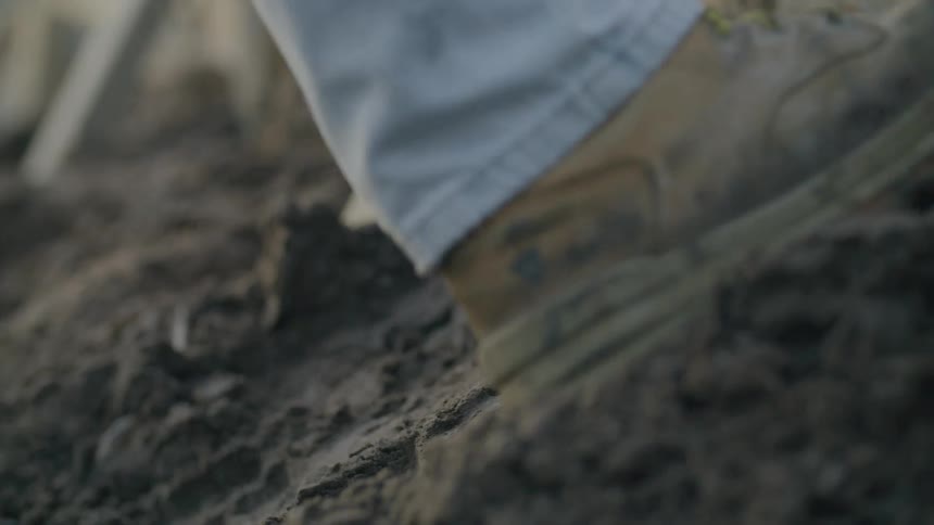 A worker tamps down dirt next to a wooden wall