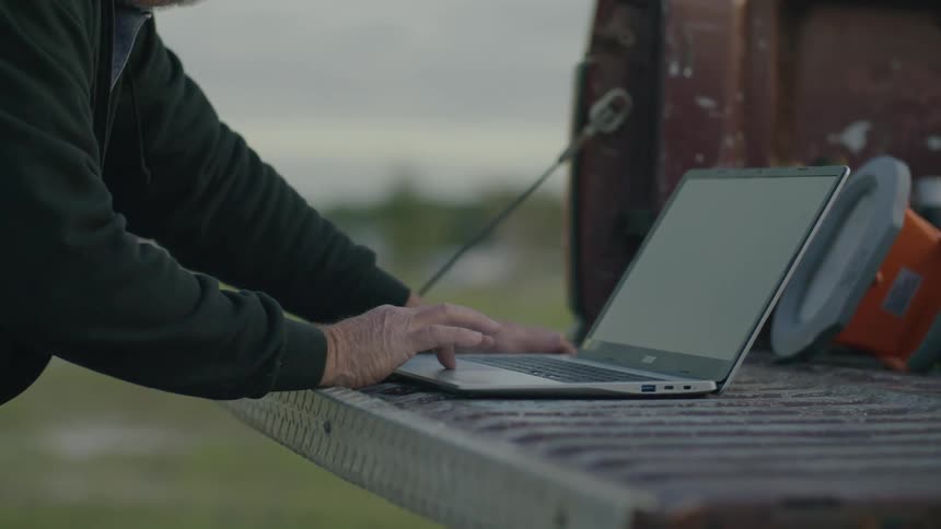 Hands of a person typing on a laptop in the back of the truck