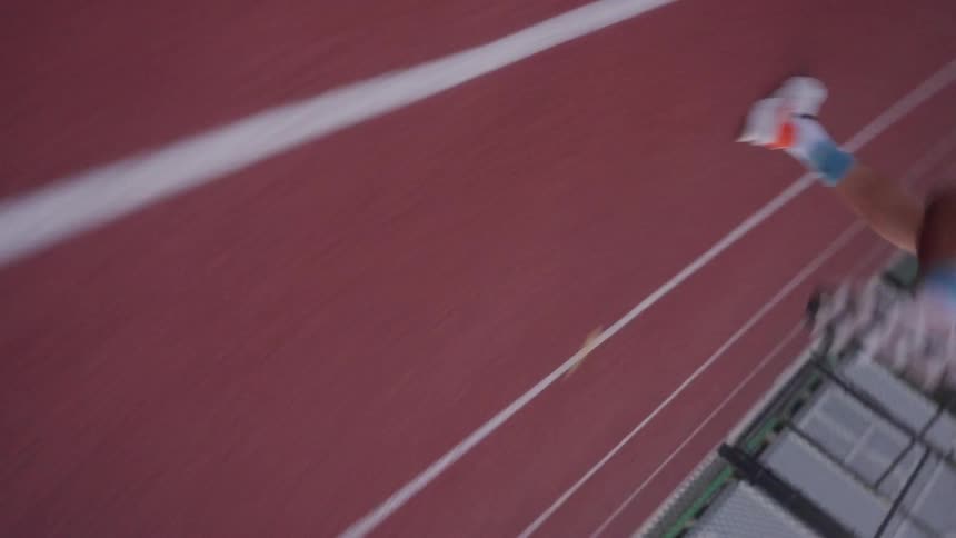 A person is running in sports shoes on a running track with a red floor