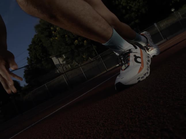 Close up slow motion runner in white running shoes taking off from starting position on race track after sundown before dark