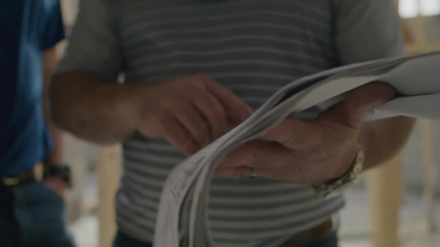 Two men look at papers inside of a partially constructed house