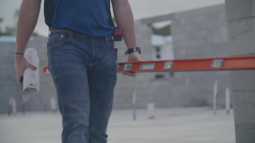 A worker carrying some tools and is walking and there are several brick walls