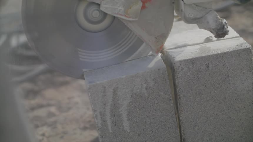 Handheld motorized circular saw blade cutting a cement block on a construction site during the day