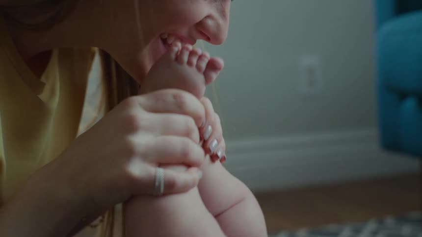 A woman is kissing the feet of a baby who is lying down and she is smiling