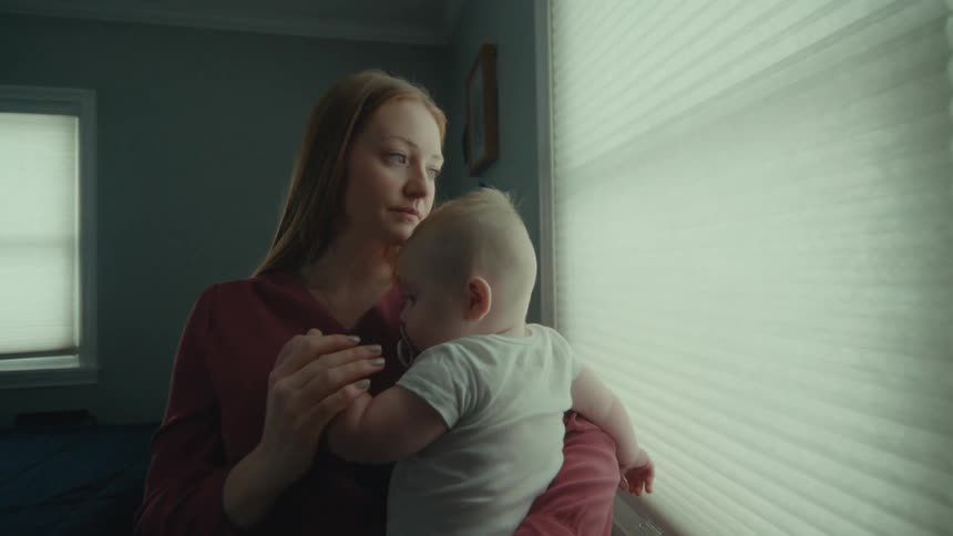 A woman looks at a window while holding her infant