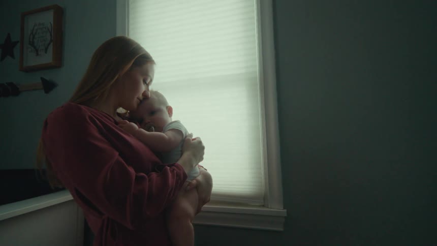 A mother hugging her baby in front of the bedroom window