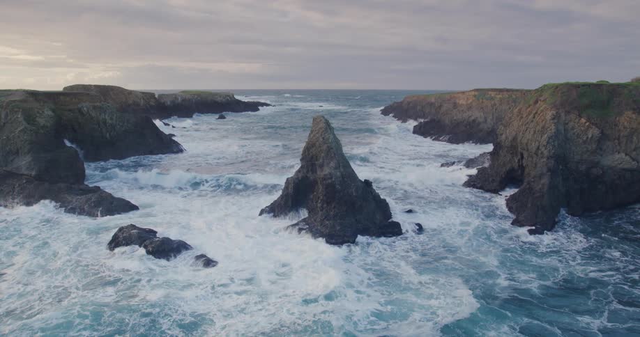 Aerial of choppy waves crashing on the mountain shore during sunset