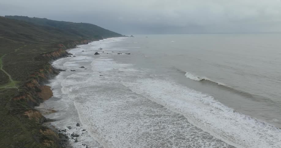 A misty view of the sea and coastal mountains under a cloudy sky