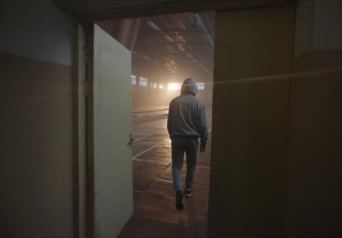 A person in a hooded jacket is walking and opens a door and walks across a sports court