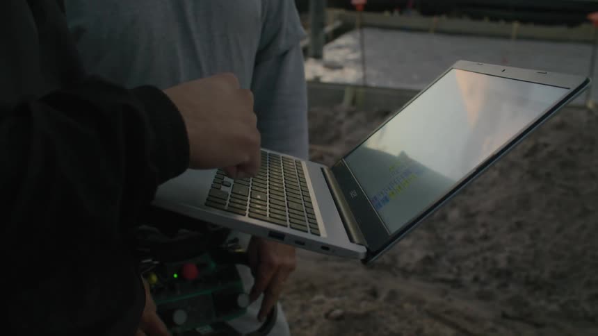 Two men use a laptop outside