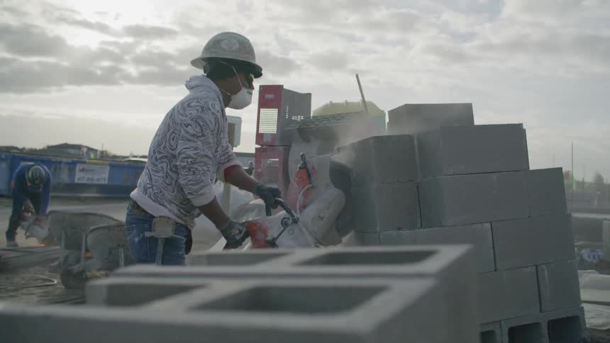 A construction worker cuts concrete blocks with a large circular saw