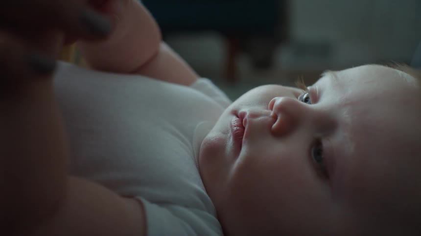 A little baby lying down with blue eyes is looking at a hand that is holding his