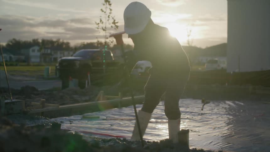 A person is wearing safety equipment and is applying cement to a construction site on the ground