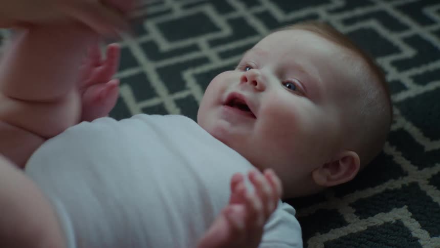 Portrait of a smiling baby lying on the carpet playing with his mother
