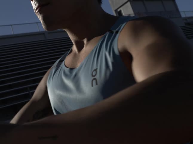 A man in a tank top is stretching his torso by rotating his arms to the sides