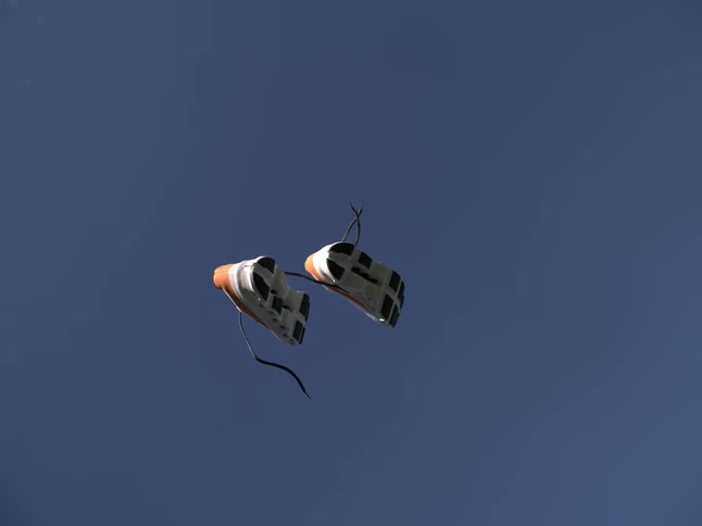 A pair of tied sneakers that are falling from the blue sky