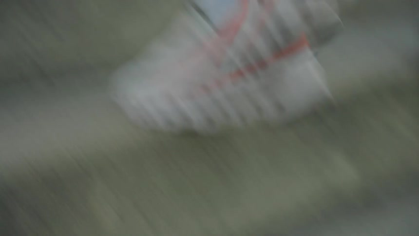 Male athlete running up cement stairs between metal bleachers wearing blue shocks and white and orange running shoes