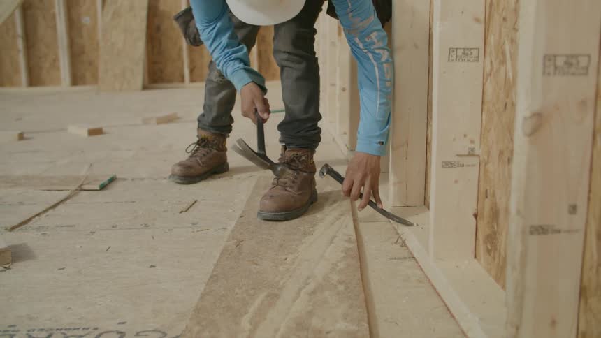 Man with a hammer drilling small holes in a wooden surface on a construction site
