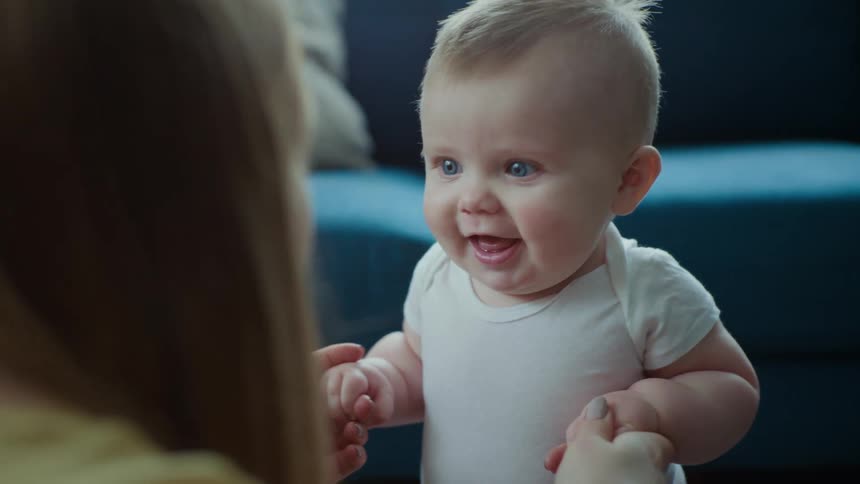 A little baby with blue eyes is looking at his mother who is talking to him and has her mouth open
