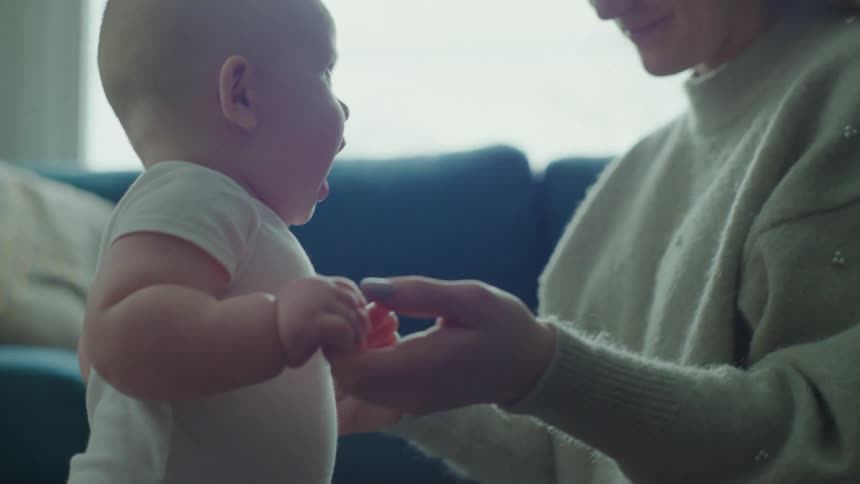 Mother holds her babys hands in a room with a blue couch
