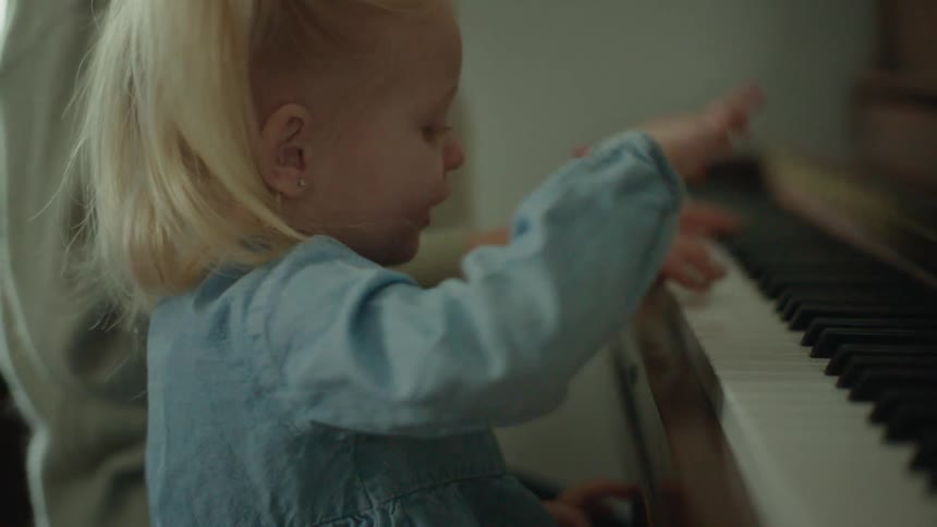 Young little girl playing the piano next to an adult