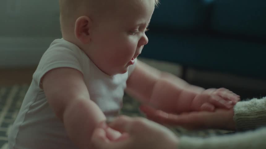 Baby sitting on the rug patting his mothers hands