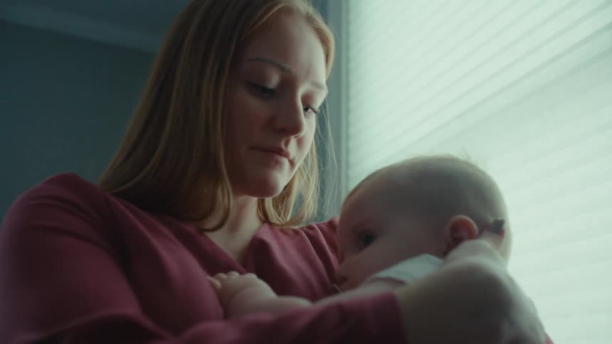 A young mother embraces her baby while it clutches her shirt