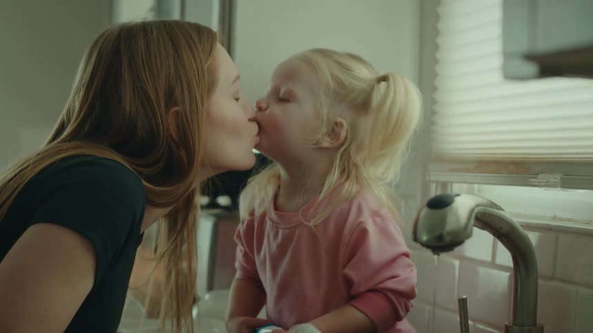 A mother kisses her daughter at the kitchen sink