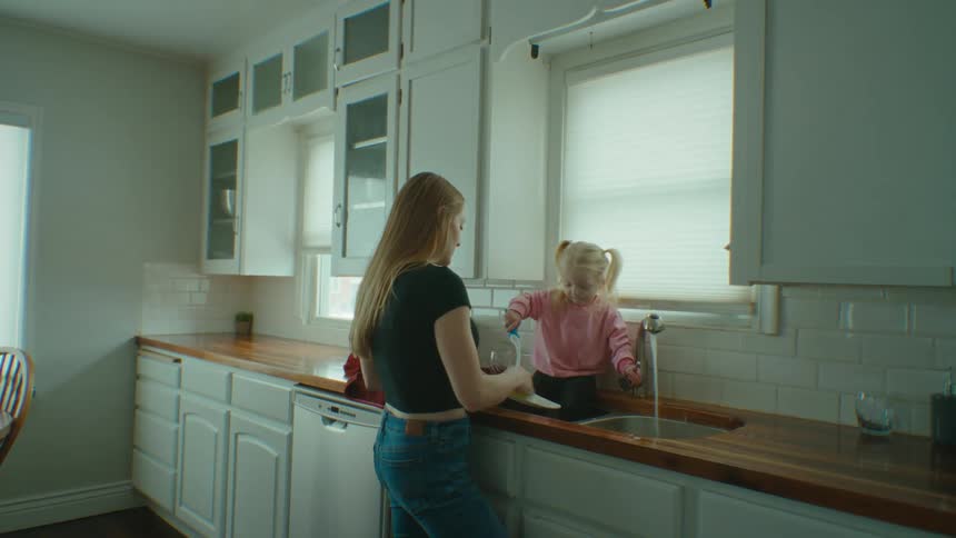 A girl helping a woman wash the dishes