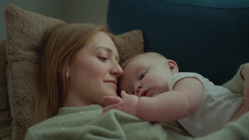 Mother lying on couch with baby smiles slightly