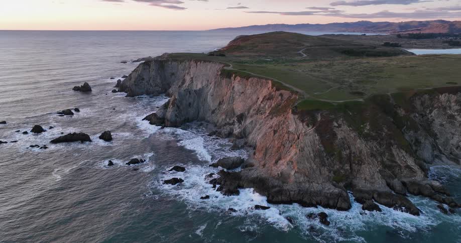 Aerial of ocean waves rolling into coastal cliffs at dusk