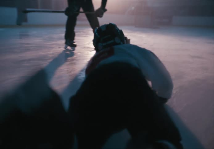 A hockey player drops and rolls on an ice rink