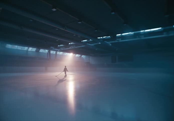 Silhouette of a solitary skater stands on the ice in a spacious and empty indoor rink