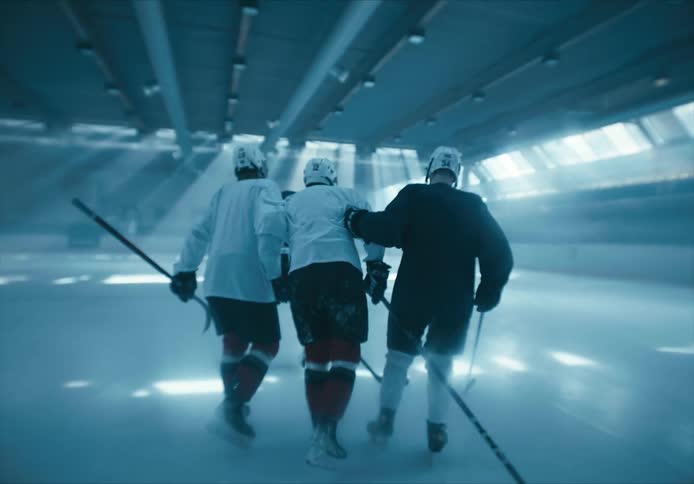 Two hockey players help another player off of the rink