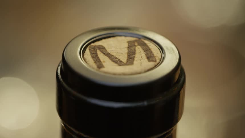 A closeup of the top of a wine bottle sealed with a cork with an m marked on it