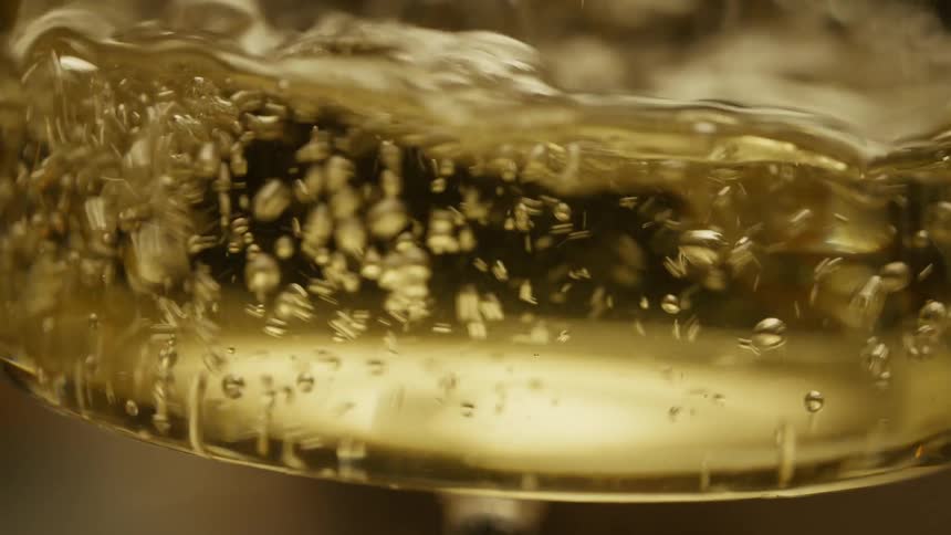 Extreme closeup on a crystal glass with alcoholic beverage liquid being poured