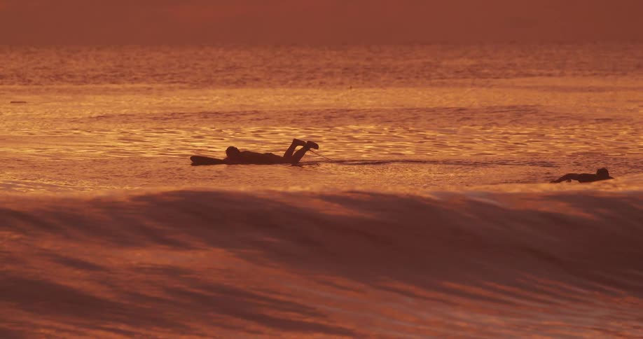 Person surfing in a sea reddened by the sky