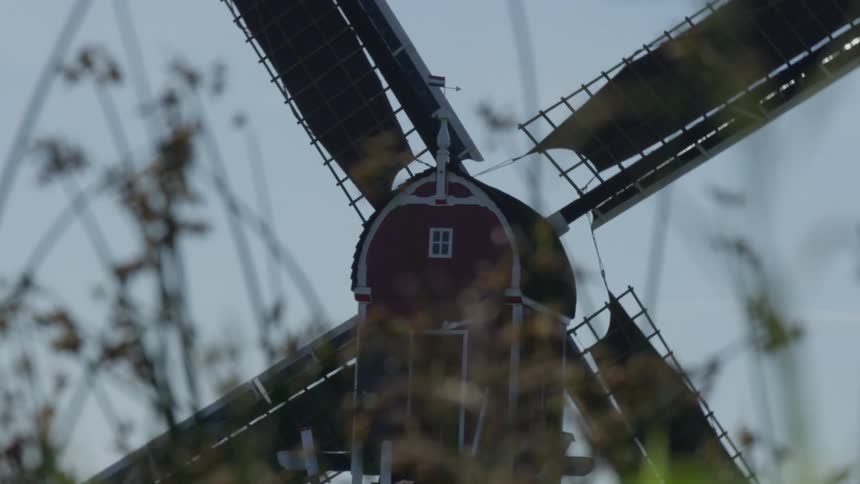 The large blades of a red windmill rotate slowly in the wind