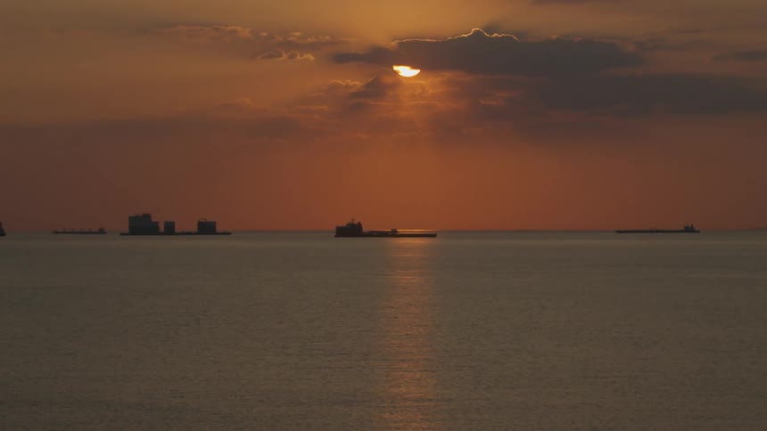 Ocean landscape with the silhouette of boats and the reddish sun on the horizon